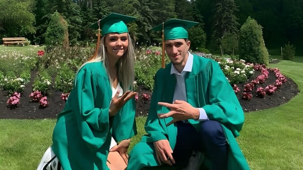 Dos estudiantes en togas de graduación verdes están en el jardín del campus del Miles Macdonell Collegiate.