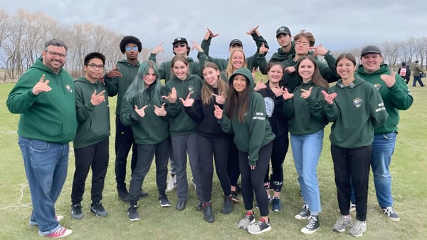 Un grupo de estudiantes del Miles Macdonell Collegiate está con sudaderas verdes en un campo al aire libre.
