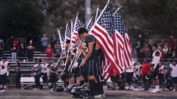 Una persona sostiene banderas americanas frente a una multitud en el terreno del Milford Public School District.