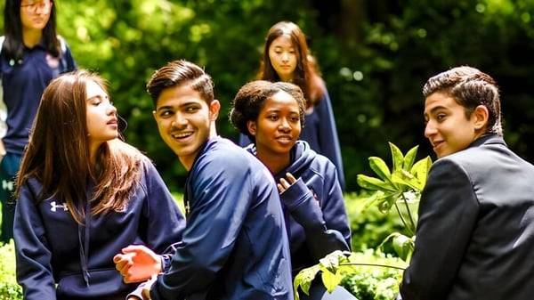 Un grupo de estudiantes en uniformes azules se reúne en el área verde exterior de la Mill Hill International.