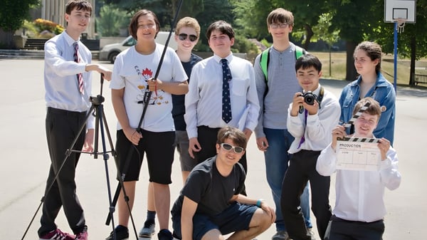 Un grupo de estudiantes de la Mill Hill School está juntos afuera cerca de una canasta de baloncesto.