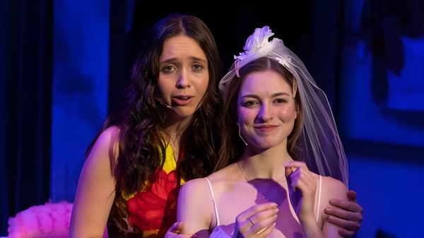Dos mujeres están juntas en un escenario con fondo azul en el campus de la Millbrook School.