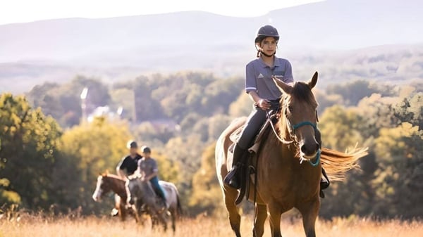 Una persona monta un caballo en un paisaje montañoso con bosque en el terreno de la Miller School of Albemarle.