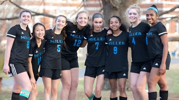 Un grupo de jóvenes atletas de la Miller School of Albemarle posan juntas al aire libre frente a árboles y edificios.