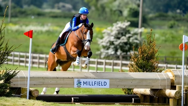 Una estudiante de la Millfield School monta a caballo con casco y ropa de protección sobre un obstáculo de madera en el campo.