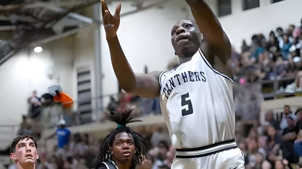 Un jugador de baloncesto de la Milton District High School salta con los brazos en alto durante un partido.