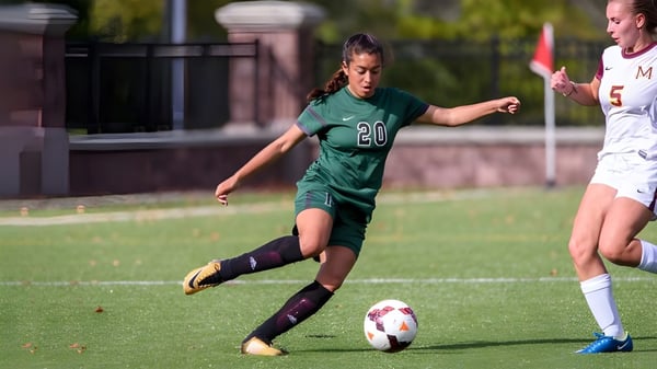 Una jugadora de fútbol vestida de verde dribla el balón en el campo de Miss Porter's School con una jugadora vestida de blanco cerca.
