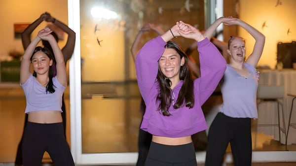 Tres alumnas de Miss Porter's School realizan ejercicios de yoga en un estudio con los brazos en alto.