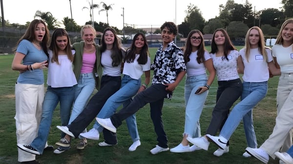 Un grupo de estudiantes está de pie en un campo de césped con palmeras en el terreno de la Mission College Preparatory Catholic High School.