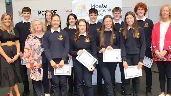 Alumnos en uniformes escolares están con certificados frente a la entrada del Moate Community College.