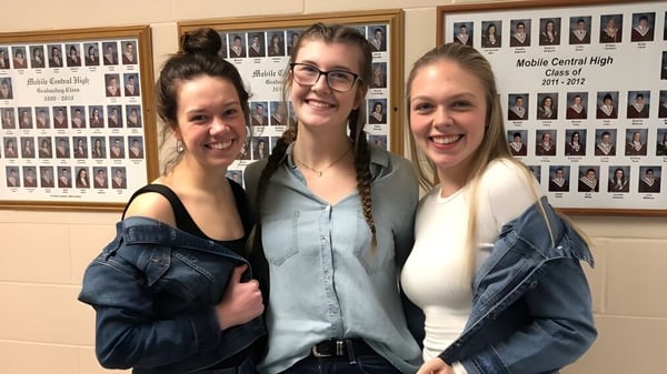 Tres estudiantes están juntos frente a una pared con fotos de clase en la Mobile Central High.