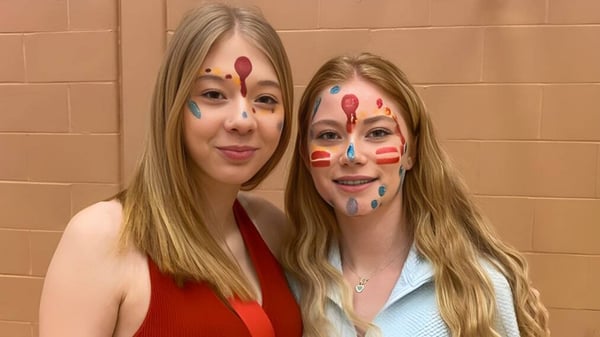 Dos estudiantes de la Mobile Central High con pintura facial colorida sonríen frente a una pared beige.