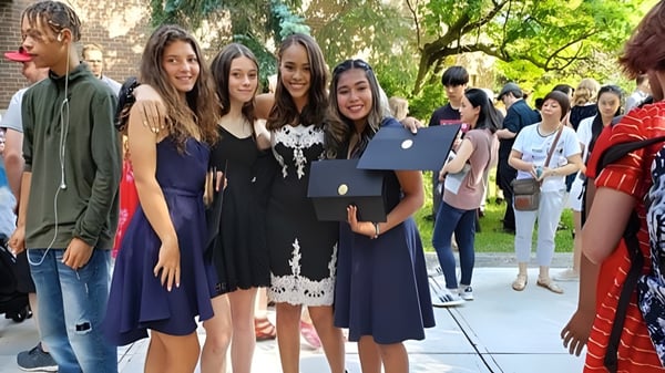 Un grupo de jóvenes graduadas está con diplomas al aire libre en el campus del Monarch Park Collegiate Institute.