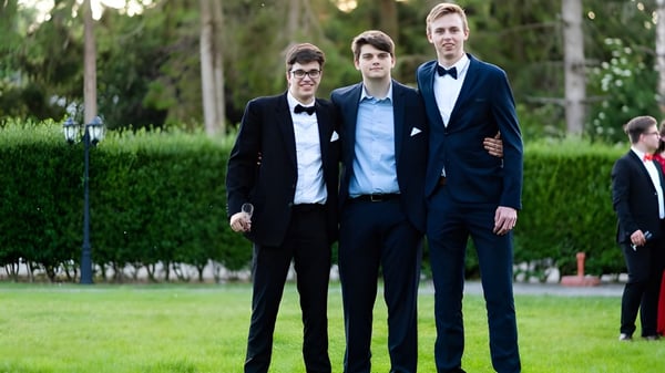 Tres estudiantes de la Monmouth School for Boys están en ropa formal en un prado frente a árboles.