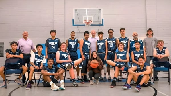 Un grupo de estudiantes de la Monterey Bay Academy posan juntos en el gimnasio frente a una canasta de baloncesto.