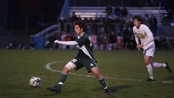 Dos estudiantes de la Montpelier High School juegan al fútbol en el campo por la noche.