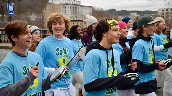 Estudiantes de la Montpelier Roxbury Public School District llevan camisetas solares azules uniformes en un entorno urbano.