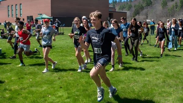 Un grupo de estudiantes se reúne en un campo deportivo frente a un edificio de ladrillo de la Montpelier Roxbury Public School District.