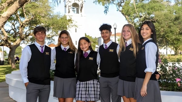 Un grupo de alumnas y alumnos posan en uniformes escolares frente al edificio del campus con campanario de la Montverde Academy.