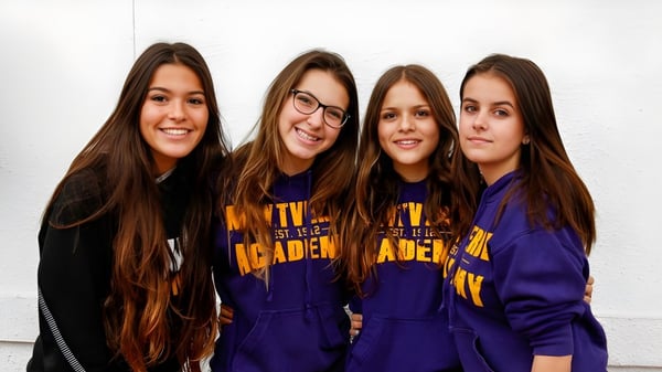 Cuatro alumnas de la Montverde Academy posan riendo frente a una pared blanca en sudaderas moradas iguales.