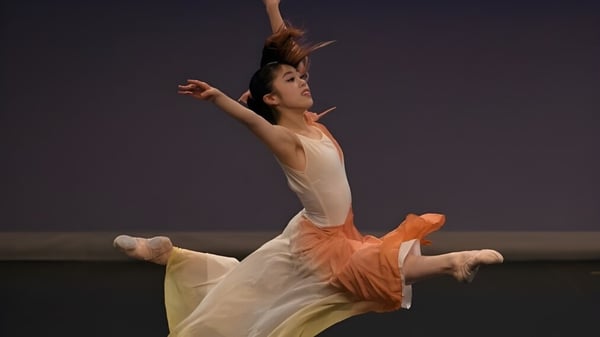 Una bailarina realiza un baile en el escenario de la Moorland School con un vestido blanco con acentos naranjas.