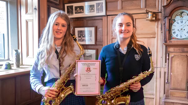 Dos alumnas de la Moreton Hall School están con saxofones en una sala con paneles de madera y un reloj antiguo en la pared.