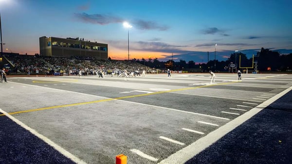 El campo de fútbol de la Morgan High School se ve al atardecer con espectadores en el estadio.