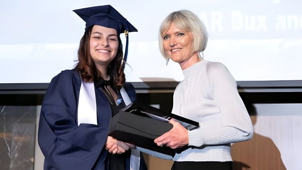 Una joven en toga está junto a una mujer mayor y sostiene un diploma en el campus de la Morley Senior High School.