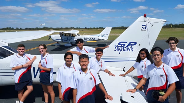 Estudiantes de la Morley Senior High School están en uniformes blancos y rojos frente al pequeño avión Sky Hawk en un campo de hierba.