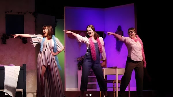 Tres alumnas de la Morro Bay High School bailan en el escenario frente a un fondo violeta.