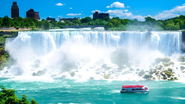 Un bote rojo con pasajeros navega frente a una cascada en el terreno de la Moscrop School.
