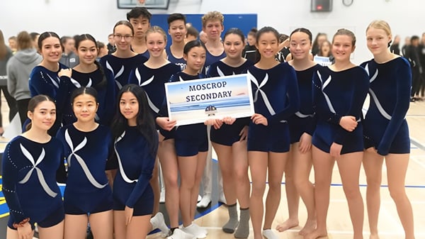 Un grupo de jóvenes estudiantes en trajes de gimnasia azules posan con un cartel que dice MOSCROP SECONDARY en la Moscrop School.