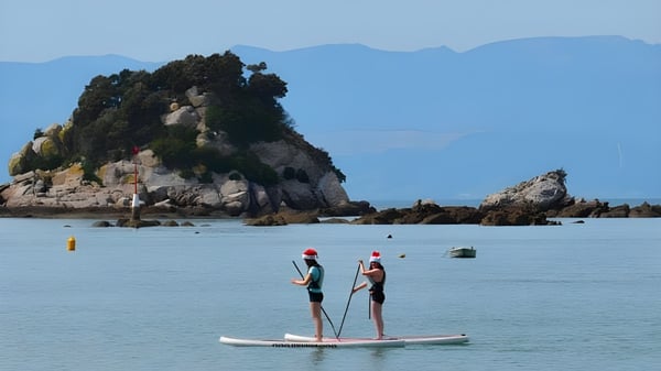 Dos personas están en paddleboards en aguas tranquilas frente al paisaje montañoso de la Motueka High School.