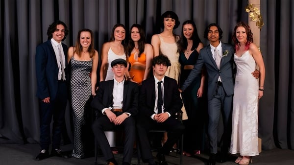 Un grupo de personas posan frente a una cortina oscura en el campus del Mount Aspiring College.