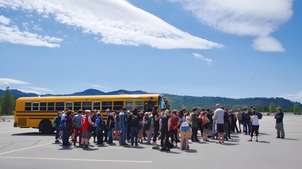 Estudiantes de la Mount Baker Secondary School están frente a un autobús escolar amarillo con montañas y un cielo azul de fondo.