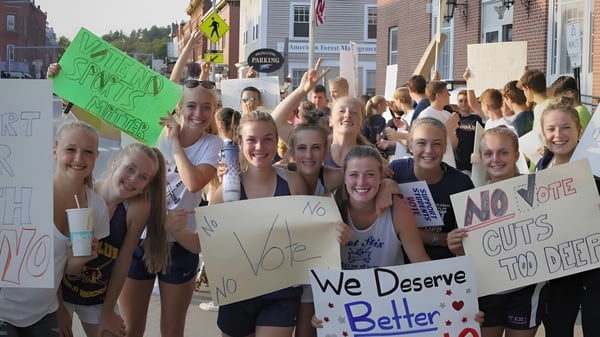 Estudiantes de la Mount Blue High School se reúnen en una calle y sostienen carteles con mensajes políticos.