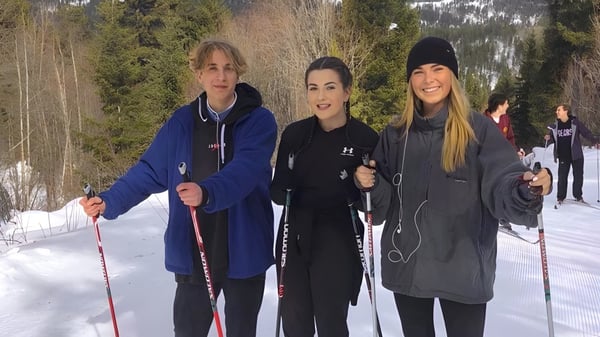 Tres alumnas de la Mount Boucherie Secondary School están en el bosque nevado sosteniendo bastones de esquí.
