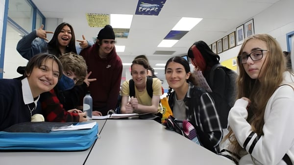 Un grupo de estudiantes de la Mount Elizabeth Middle/Secondary School se sienta alrededor de una mesa en el aula y trabaja juntos.