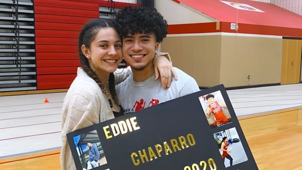 Una joven pareja posa junta frente a un cartel con el nombre Eddie Chaparro en el campus de la Mount Everett Regional High School.