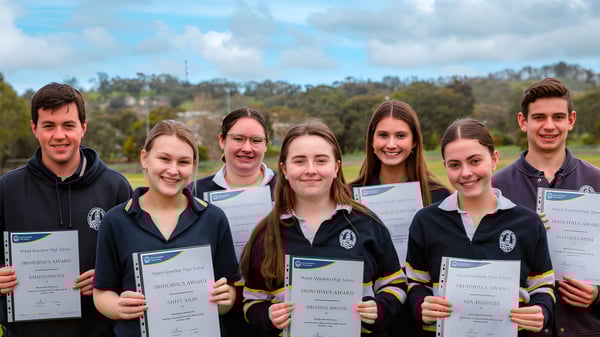 Estudiantes de la Mount Gambier High School muestran al aire libre sus certificados frente a árboles y edificios escolares.