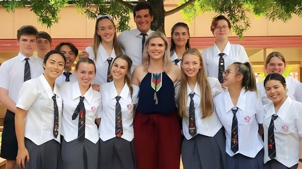 Un grupo de estudiantes de la Mount Gravatt State High School está en un aula con un árbol verde de fondo.