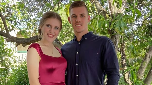 Una joven pareja sonriente está afuera en el campo del campus de la Mount Gravatt State High School.