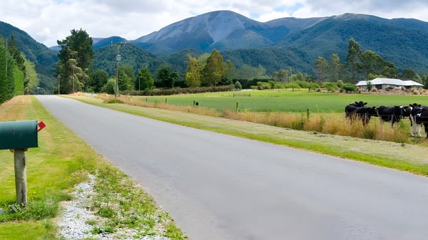Una carretera de grava serpentea a través de un prado verde con vistas a montañas cubiertas de nieve y bosques densos en el terreno del Mount Hutt College.