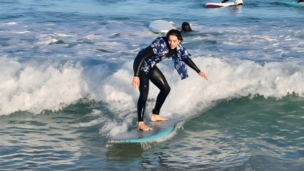 Una persona en un traje de neopreno surfa una ola en el océano frente a la costa de la Mount Lawley Senior High School.