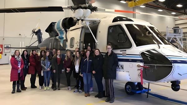 Un grupo de estudiantes de la Mount Pearl Senior High School está frente a un gran helicóptero blanco en una sala de exhibición.