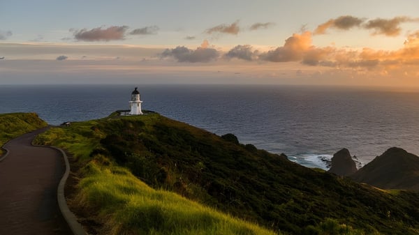 Un faro se encuentra en un acantilado cubierto de hierba junto al mar en el terreno de la Mount Roskill Grammar School al atardecer.