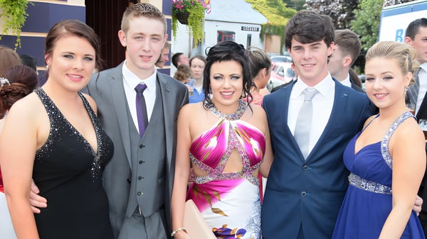 Un grupo en ropa formal posa en un evento en el campus de la Moyne Community School frente a edificios y áreas verdes.