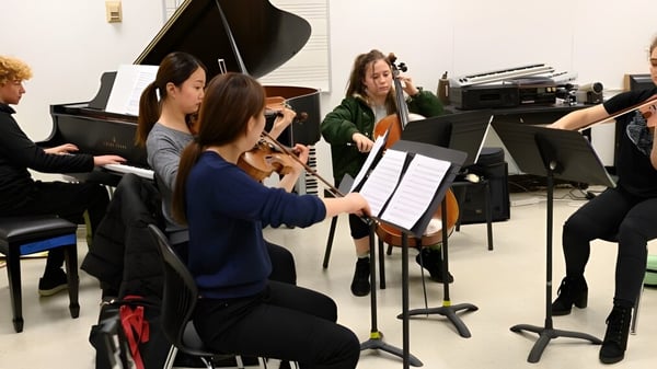 Un grupo de estudiantes de la Moyne Community School ensaya juntos con instrumentos musicales en una sala.