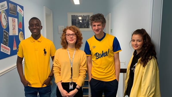 Cuatro estudiantes están juntos en un aula de MPW Birmingham frente a carteles informativos.