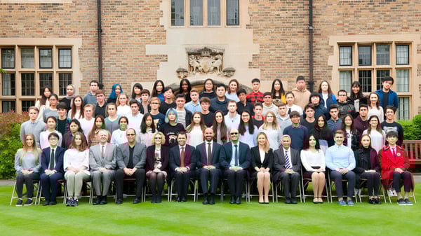 Un grupo de estudiantes está de pie y sentados frente a un edificio de ladrillo en el campus de MPW Cambridge.